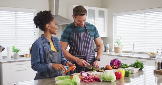 Image of happy diverse couple preparing meal, cutting vegetables in kitchen. Love, relationship and spending quality time together at home.