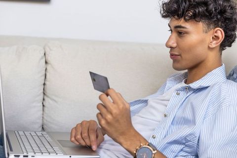 Young Man Shopping Online Using Credit Card on Laptop in Living Room