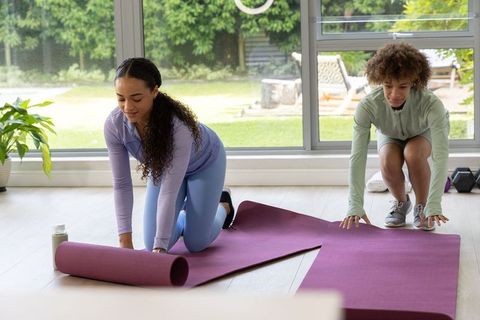 African american women unrolling purple yoga mats in sunlit living room for home workout
