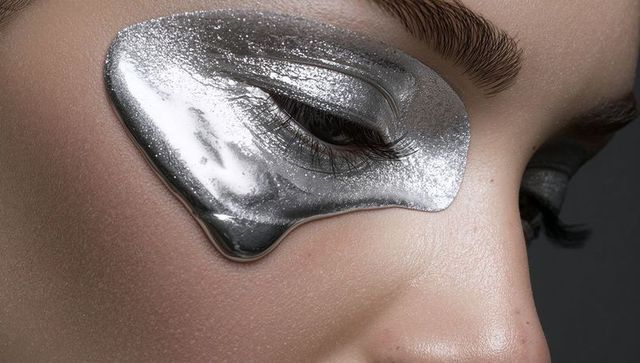 Woman wearing glossy silver under-eye mask with metallic eyelid makeup and long lashes