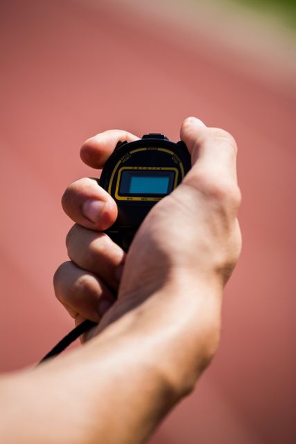 Close-up of a hand holding a stopwatch on a running track. Ideal for illustrating concepts related to sports timing, athletic training, fitness routines, and competitive racing. Useful for sports event promotions, fitness blogs, and athletic training guides.