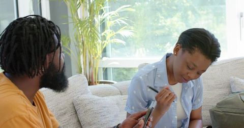 Couple studying together man holding smartphone while woman writing notes on sofa