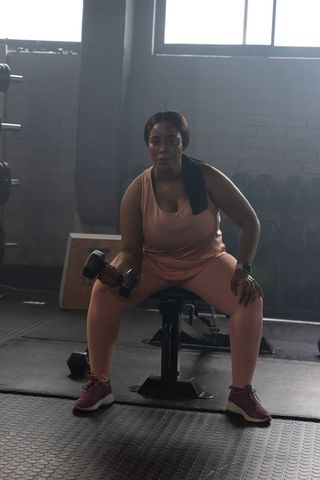 Plus-size african american woman strength training with dumbbell on bench in urban gym