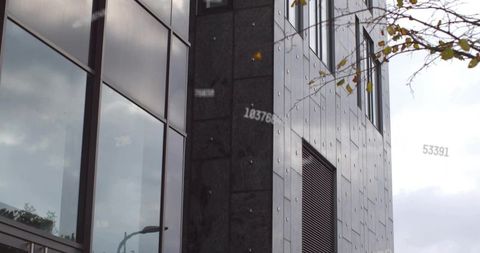 Reflecting clouds on glass facade with dark metal cladding and vent, urban foliage