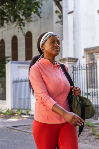 African woman walking confidently in pink activewear carrying green gym bag in city