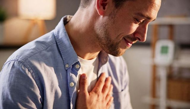 Man holding hand to chest, smiling in cozy home interior, expressing gratitude and relief