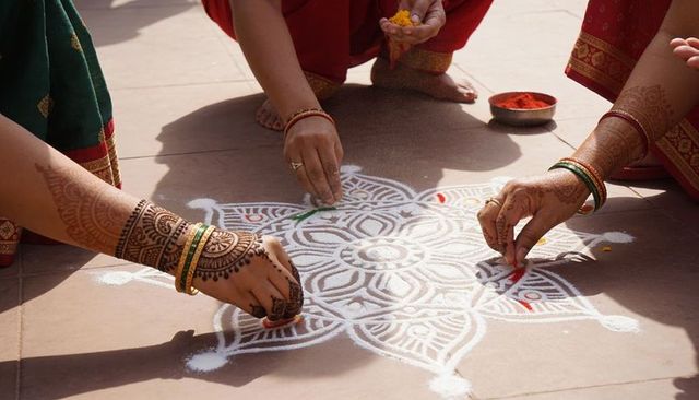 Indian women creating intricate rangoli with colored powder and mehndi on tiled courtyard
