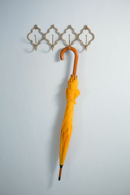 This image showcases a yellow umbrella hanging on a decorative hook against a white wall, perfect for illustrating concepts of home organization, minimalist decor, and modern interior design. It can be used in articles or advertisements related to home improvement, storage solutions, or rainy day essentials.
