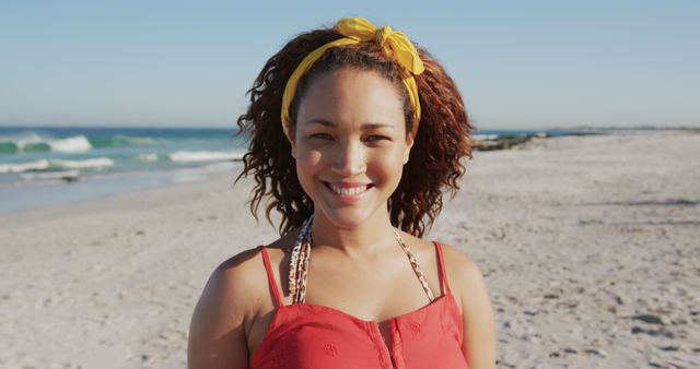 Cheerful woman with curly hair, wearing headband, enjoying day at beach with ocean in background. Perfect for promoting summer vacations, beachwear, travel destinations, or lifestyle blogs.