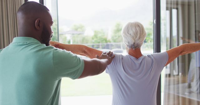 Image of back view of african american male physiotherapist exercising with caucasian senior woman. seniors health and nursing home lifestyle concept.