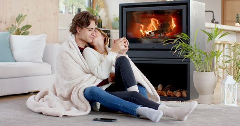 Romantic Couple Relaxing by Cozy Fireplace with Hot Drinks