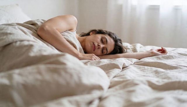 Sleeping woman in neutral linen bedding conveying calm morning light and restful wellness
