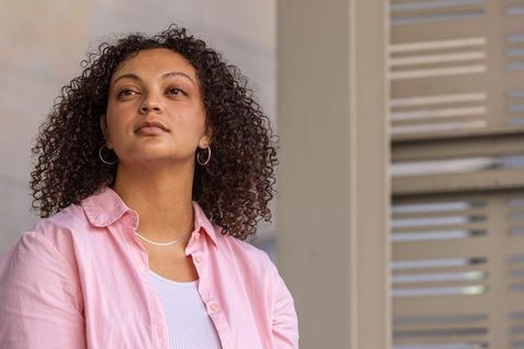 Confident african american woman standing, gazing upward in pink shirt with hoop earrings