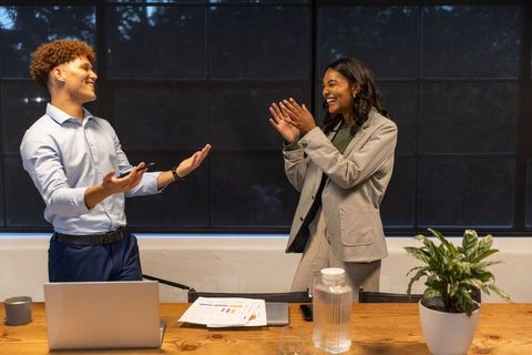Diverse coworkers celebrating successful presentation in modern office conference room