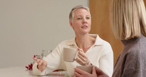 Mature women chatting over coffee at kitchen table enjoying cozy conversation and companionship
