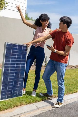 Diverse couple evaluating residential solar panel curbside using smartphone and smartwatch