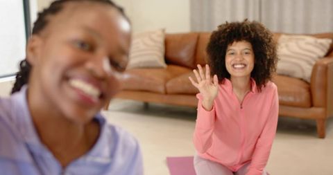 Smiling women waving during home yoga session on pink mat, casual fitness friendship