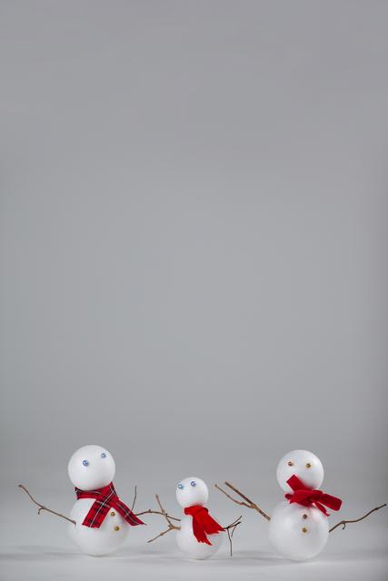 Three Christmas snowman ornaments with red scarves are standing against a white background. The snowmen are arranged in a row, with twig arms and button eyes, creating a festive and cheerful atmosphere. This image is perfect for holiday greeting cards, seasonal advertisements, winter-themed decorations, and festive social media posts.