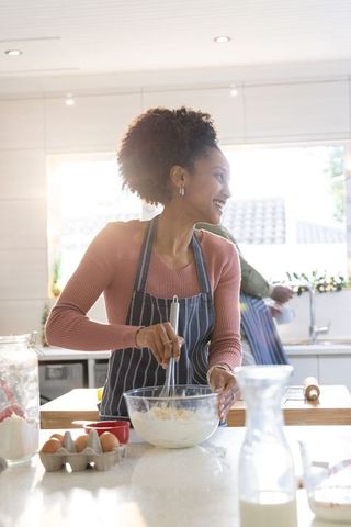 Black woman whisking batter in bright home kitchen wearing striped apron, joyful baking
