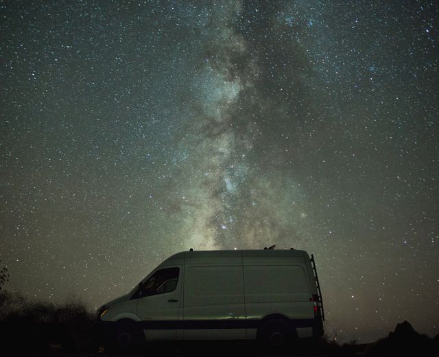 Capturing serene night scene with van and star-filled sky featuring majestic Milky Way. Ideal for promoting adventure travel, off-grid camping, van life, or astronomy content. Evokes feelings of peace, wonder, and freedom.