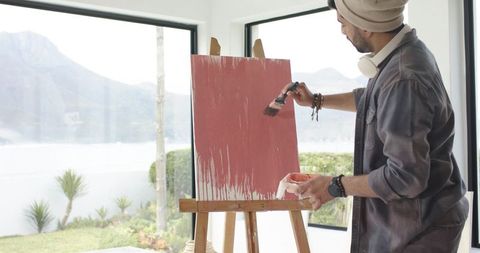 Indian artist painting crimson strokes on canvas in sunlit studio overlooking bay