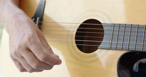 Senior man plucking acoustic guitar strings closeup showing hand, sound hole and fretboard