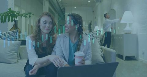 Two women discussing fintech analytics on laptop with candlestick overlay, coworking lounge
