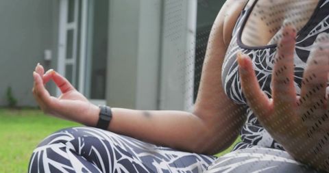 Woman meditating on lawn wearing patterned activewear and fitness watch for urban wellness