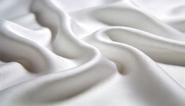 Shimmering white satin fabric with soft flowing folds and glossy highlights for luxury textiles