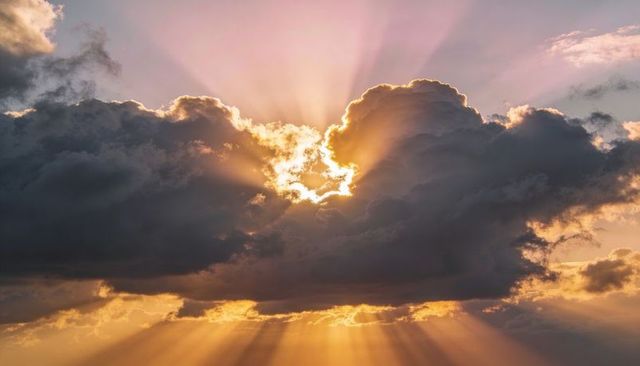 Golden sunburst breaking through dramatic cumulus clouds at sunrise with pink glow