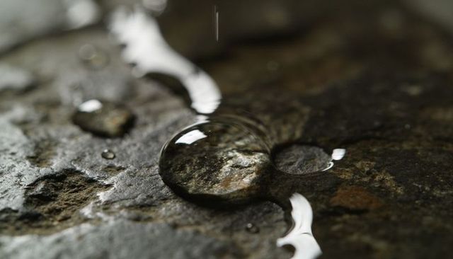 Single water droplet clinging to textured wet slate surface with reflective macro detail