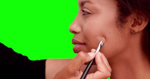 Makeup artist applying foundation on model against green background