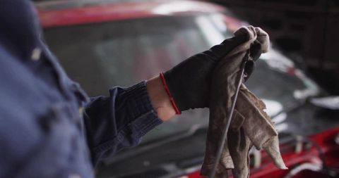 Mechanic inspecting and wiping engine oil dipstick with gloved hand and rag at repair bay