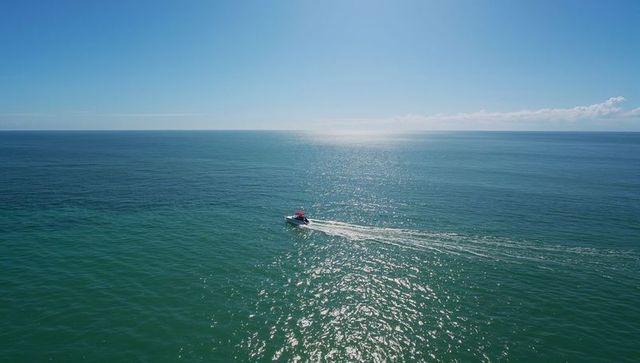 Small Motorboat Cruising Across Sunlit Open Ocean with Red Canopy and Glittering Wake