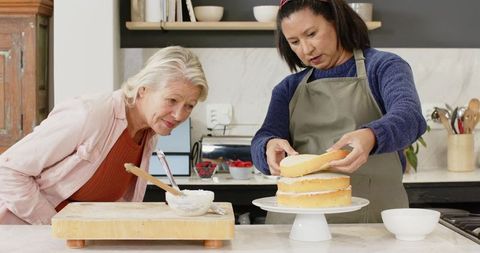 Senior women collaborating to assemble layer cake in cozy kitchen