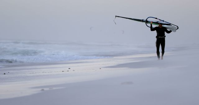 Person Carrying Windsurfing Board on Misty Beach - Download Free Stock Images Pikwizard.com