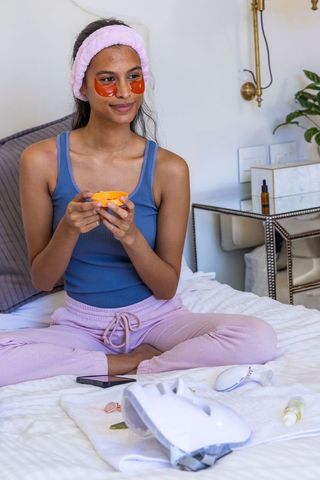 Young woman enjoying at-home skincare routine with eye hydrogel patches and moisturizer