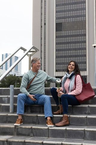 Middle-aged couple sharing daisies on urban steps near highrise office building