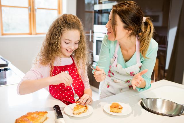 Mother and daughter eating pancake in kitchen at home