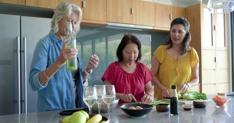 Diverse friends preparing dinner at modern kitchen island with wine and fresh vegetables