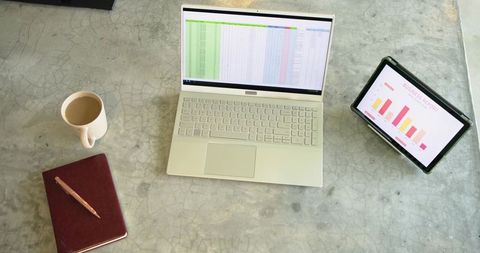 Minimalist workspace showing laptop with spreadsheet and tablet displaying bar charts