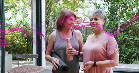 Mature women smiling after outdoor yoga holding mat and bottle on garden patio poolside