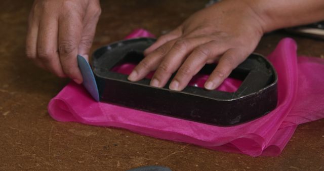 Close-up view of hands working on cutting pink fabric using a template. This could be ideal for illustrating articles or guides on sewing, tailoring, fabric crafting, or DIY fashion projects. Suitable for use in educational materials, websites focusing on creative arts, and tutorials for beginners in fashion design.