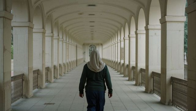 Woman walking under neoclassical arched colonnade wearing headscarf and hoodie