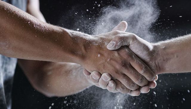 Chalk explosion handshake between athletes gripping firm forearms showing strength