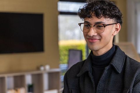 Smiling young man wearing tortoiseshell glasses and turtleneck sitting in modern lounge