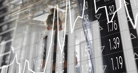 Female financial analyst studying overlaid charts through glass partition in modern office