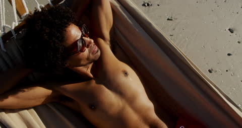 Relaxed Young Man Sunbathing in Beach Hammock at Sunset