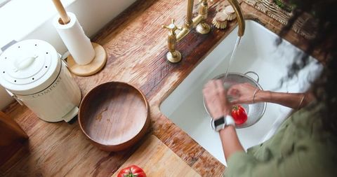 Woman washing tomato in rustic kitchen with brass faucet