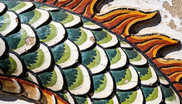 Weathered ceramic dragon scales mosaic with colorful flame border showing patina and chips